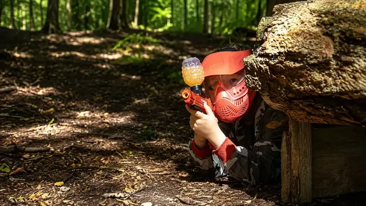 A child in a mask firing a Gelball blaster from cover