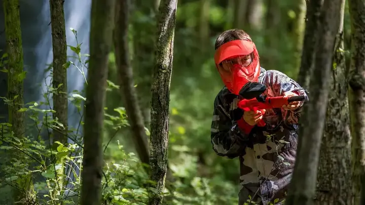A young player in a red mask peering round a tree