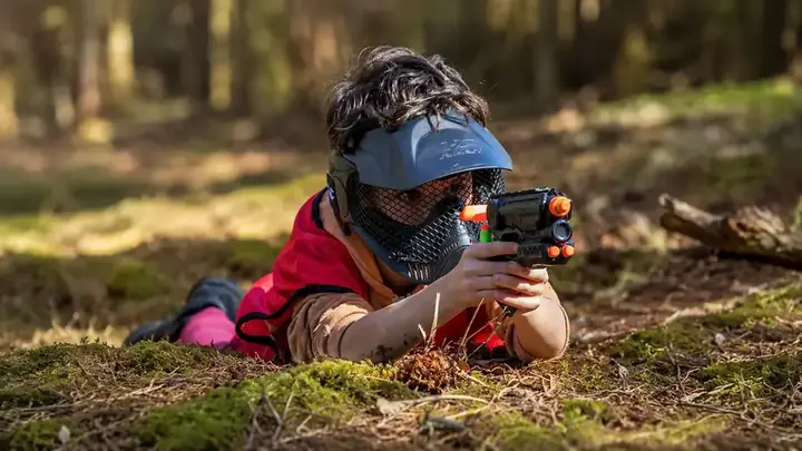 A child crouching with a blaster in the woods