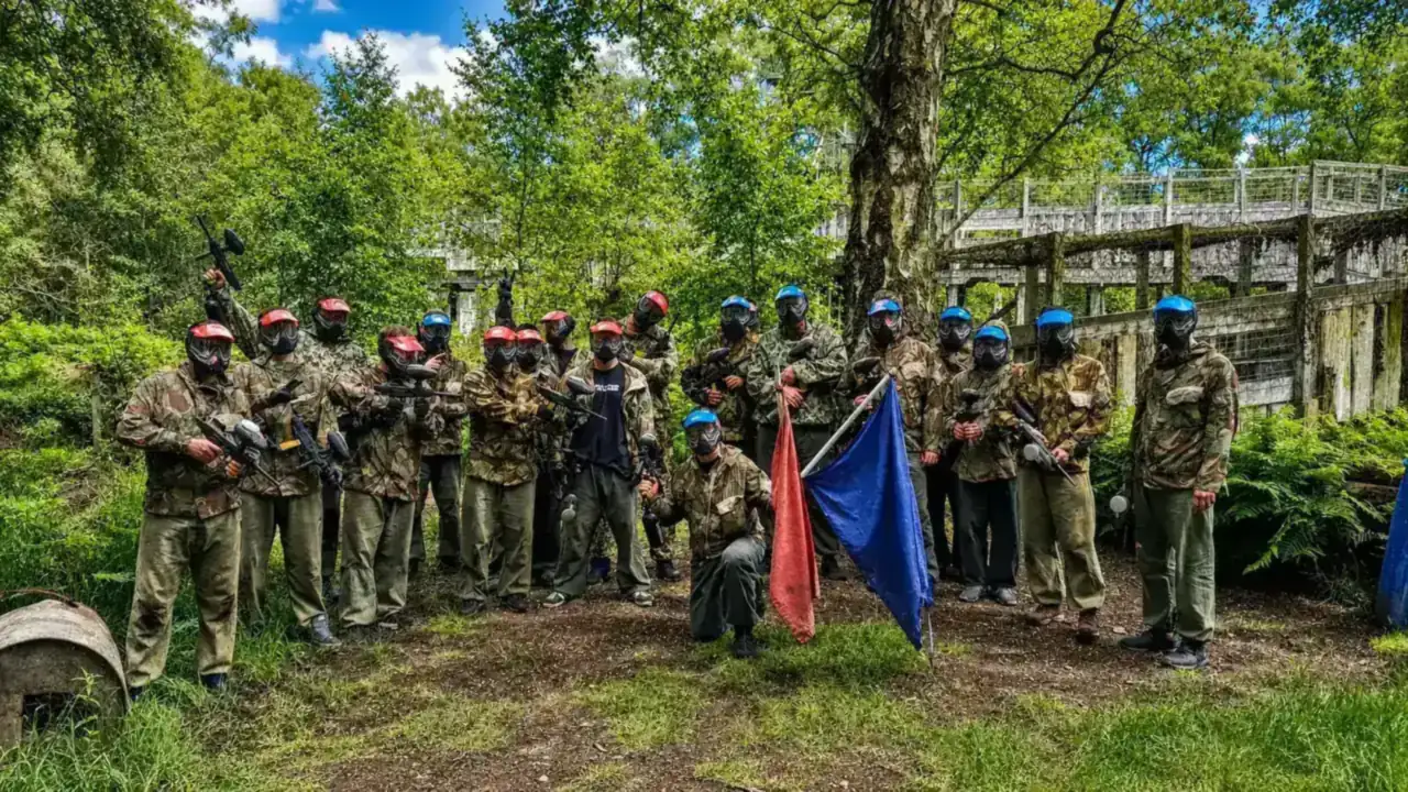 A large group in paintball kit with red and blue team flags